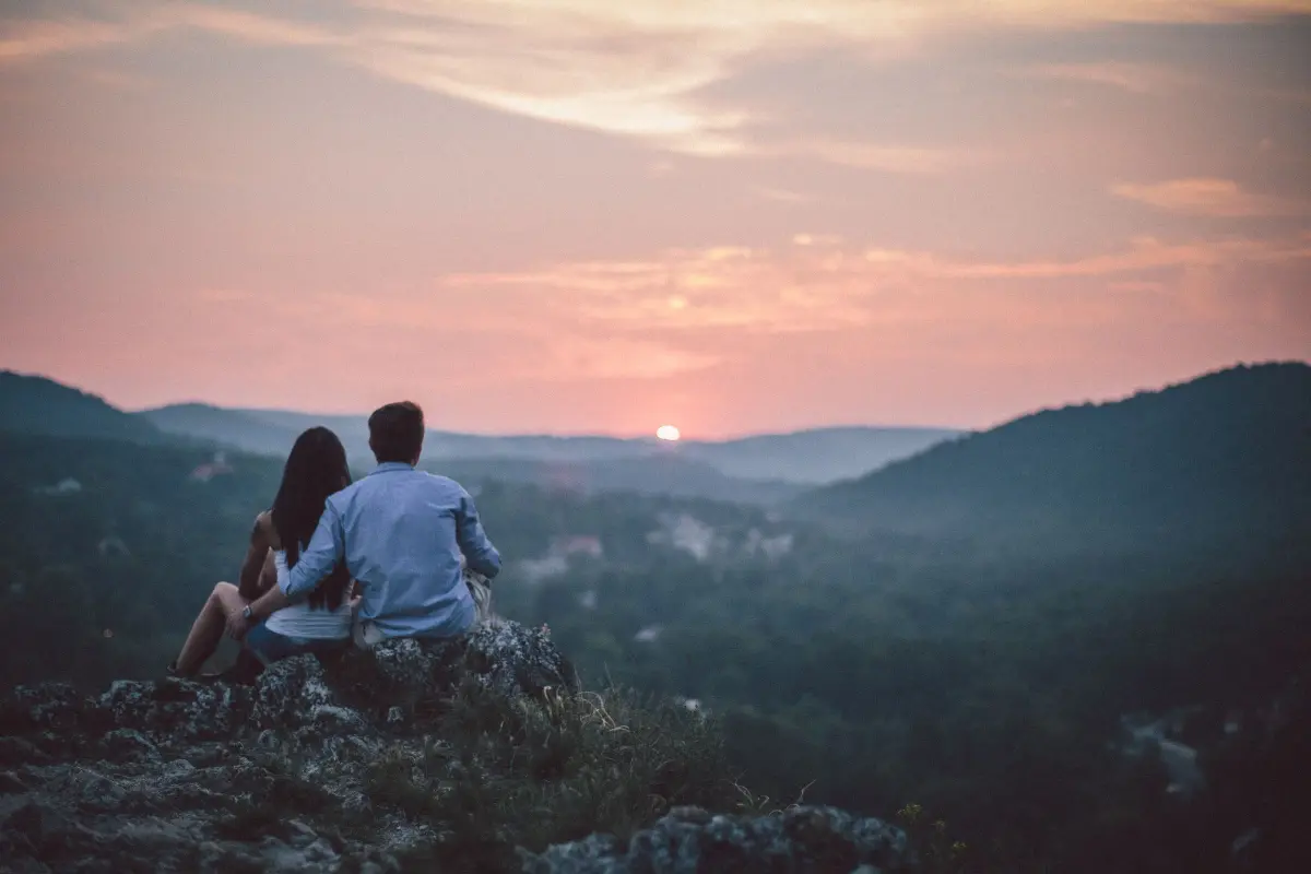 Due viaggiatori seduti su una roccia a guardare il tramonto sulle montagne